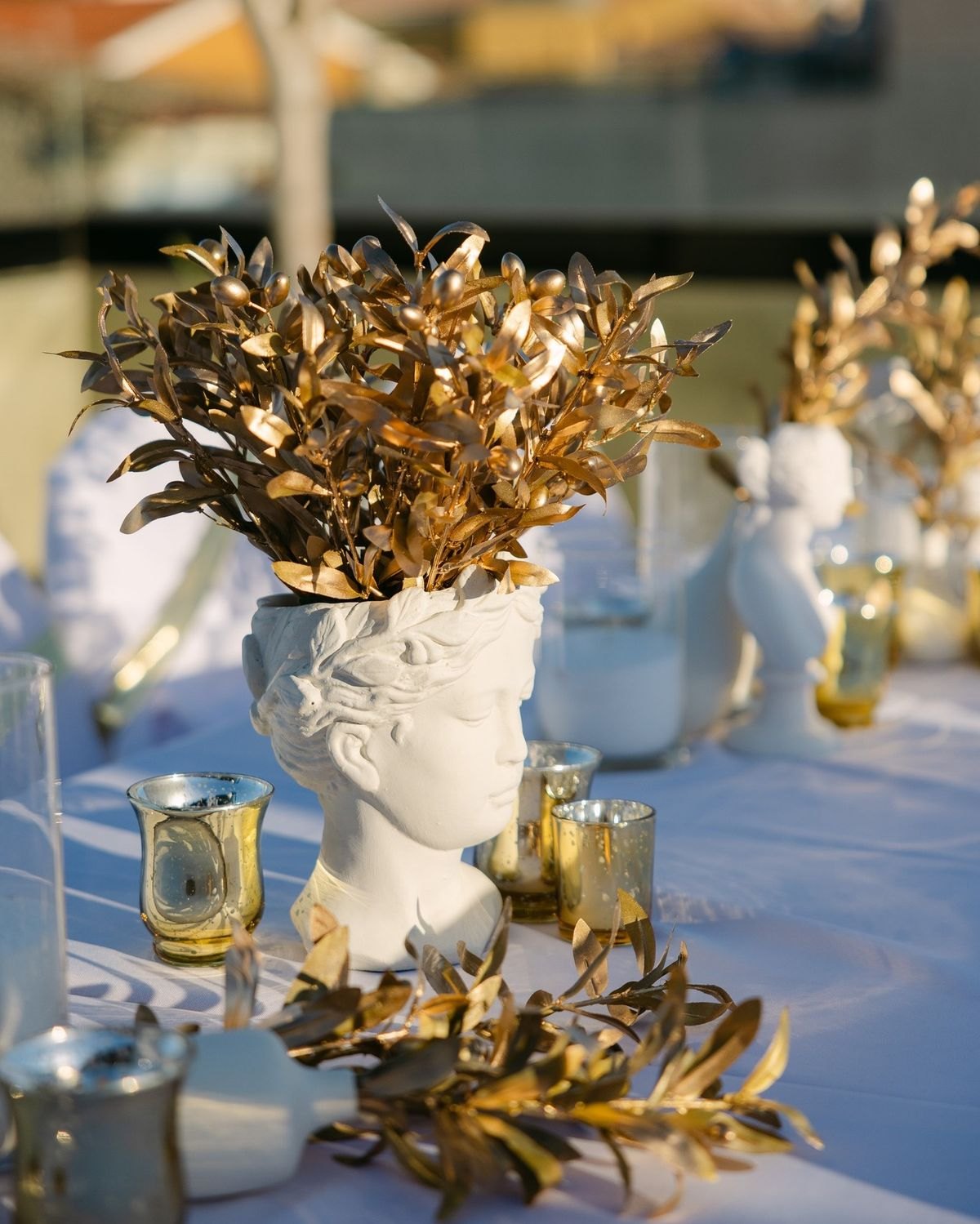 Ivory bust vase with gold foliage and gold glassware on a dressed banquet table