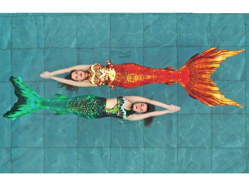 Two mermaid-costumed swimmers performing in a pool